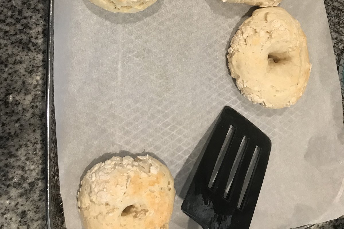 Accessoires air fryer : bagels cuits sur du papier cuisson, avec une spatule (photo d’illustration)