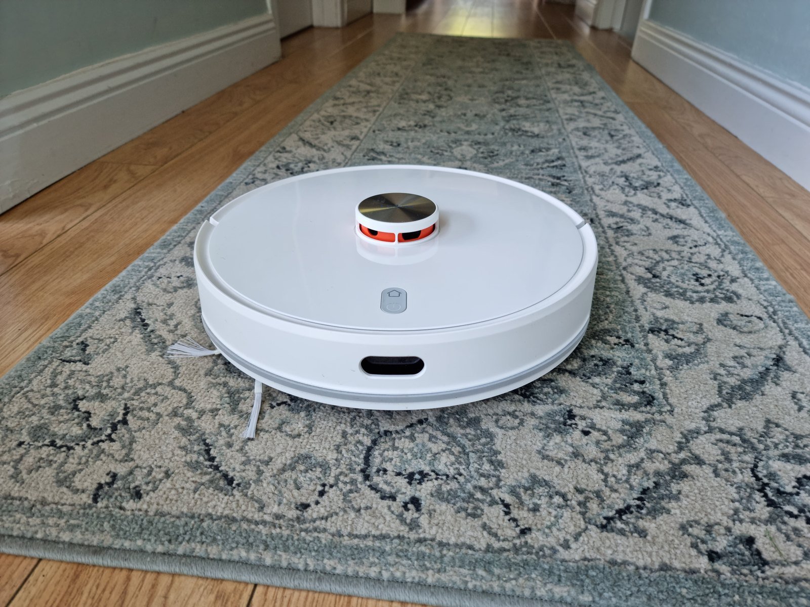Aspirateur robot laveur avec station complète : robot aspirateur blanc à capteur laser sur un tapis de couloir (photo d’illustration)