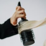 Brosse soufflante rotative : une main enroule une mèche de cheveux blonds autour d’une brosse ronde noire (photo d’illustration)