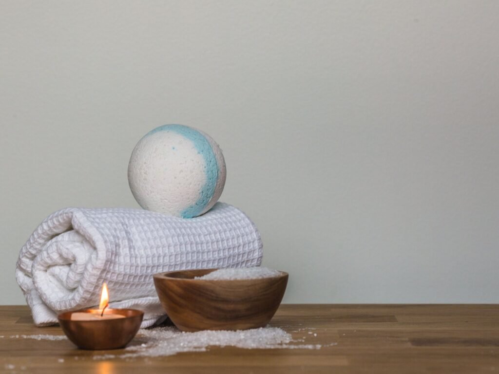Cadeau de Noël pour femme : serviette roulée, bombe de bain, bougie et bol de sels de bain sur une table en bois (photo d’illustration)