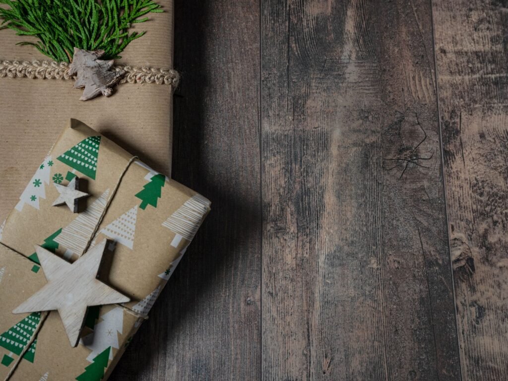Cadeau pour homme qui a tout : paquets en papier kraft avec ficelle, étoile en bois et branche de thuya sur un plancher en bois sombre (photo d’illustration)