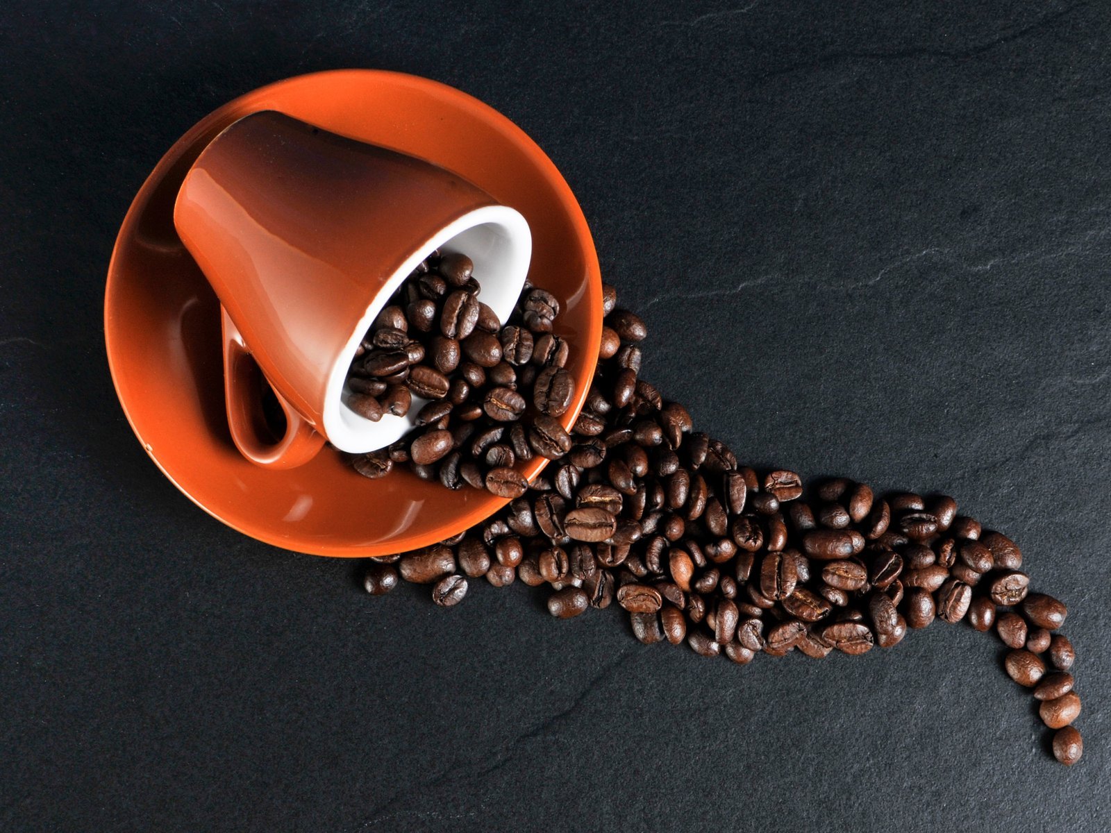 Machine à café à grain : grains de café torréfiés qui s’échappent d’une tasse à expresso posée sur sa soucoupe (photo d’illustration)