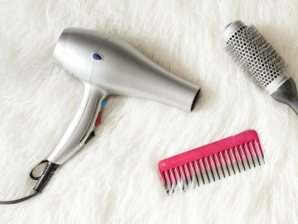 Sèche-cheveux silencieux : un sèche-cheveux gris posé sur un plaid blanc, à côté d’un peigne et d’une brosse ronde (photo d’illustration)