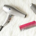 Sèche-cheveux silencieux : un sèche-cheveux gris posé sur un plaid blanc, à côté d’un peigne et d’une brosse ronde (photo d’illustration)